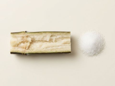Aufgeschnittenes Zuckerrohr neben feinen weissen Kristallen