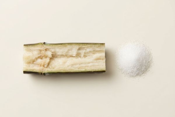 Aufgeschnittenes Zuckerrohr neben feinen weissen Kristallen